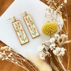 two pairs of beaded earrings sitting on top of a piece of paper next to dried flowers