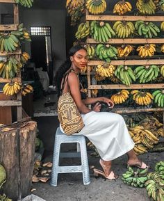 a woman sitting on a stool next to bunches of bananas