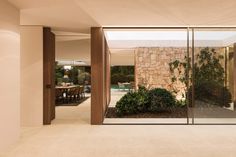 the inside of a house with glass walls and plants in the front yard, as well as an outdoor dining area