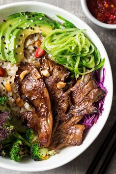 a white bowl filled with meat, broccoli and rice next to chopsticks