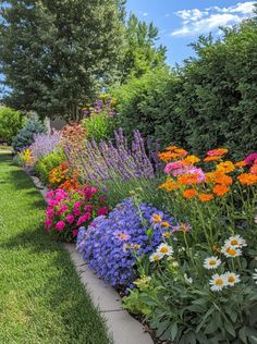 a garden filled with lots of colorful flowers next to green grass and trees on a sunny day