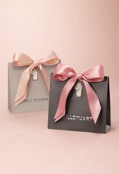 two small gift bags with pink bows on the front and grey one in the back