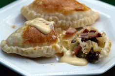 two pastries on a white plate covered in cheese and toppings, with sauce drizzled over them