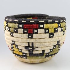 a close up of a basket on a white surface with red, yellow and black designs