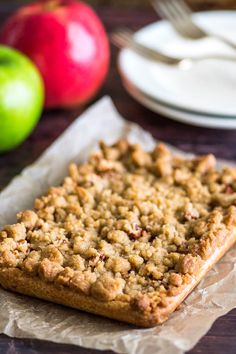 an apple pie sitting on top of a piece of wax paper next to some apples