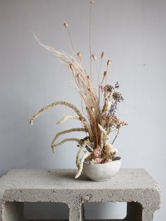 a white bowl filled with lots of flowers on top of a cement block table next to a wall