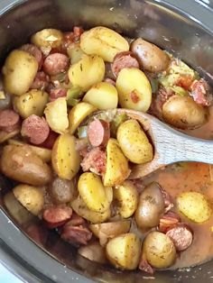 a pot full of potatoes and sausage with a wooden spoon