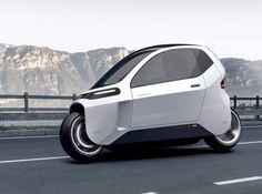 an electric car is driving on the road near some mountains and hills in the background