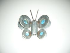 a close up of a butterfly brooch on a white surface with blue stones in the center