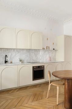 a kitchen with white cabinets and wood flooring next to a wooden table in front of an oven