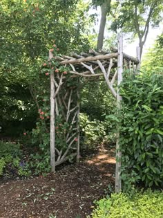 a wooden arbor in the middle of a garden with shrubs and trees around it,