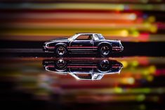 a toy car sitting on top of a table next to a reflection in the water