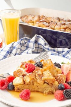 a white plate topped with french toast and berries next to a glass of orange juice