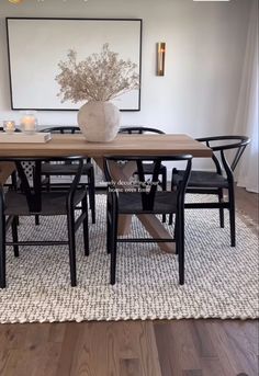 a dining room table with chairs and a vase on top of it in front of a painting