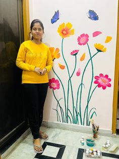 a woman standing in front of a wall with flowers painted on it