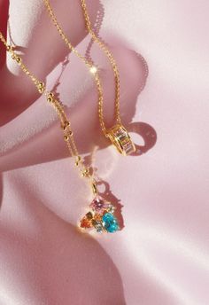 two necklaces with different colored stones are on a pink cloth, one is gold and the other is silver