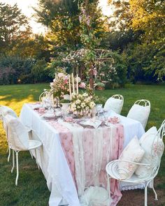 a table set up with white chairs and pink flowers