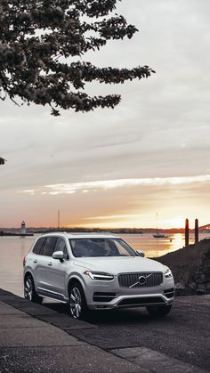 a white volvo suv is parked on the side of the road by the water at sunset