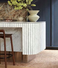 a vase with flowers sitting on top of a marble counter next to two stools