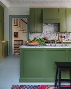 a kitchen with green cabinets, marble counter tops and wooden stools in front of the sink