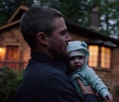 a man holding a baby in front of a house