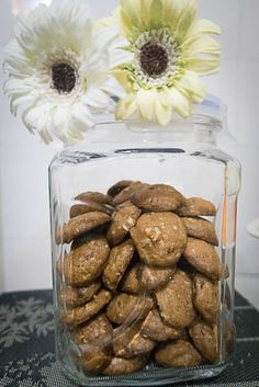 a glass jar filled with cookies next to two white flowers on top of a table