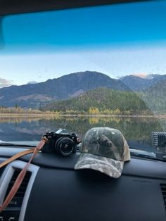 there is a hat and camera on the dashboard of a car with mountains in the background