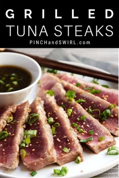 grilled tuna steaks served on a white plate with dipping sauce and green onions