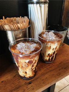 two glasses filled with ice cream sitting on top of a wooden table next to drinks