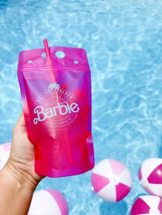 a person holding up a pink plastic drink in front of a pool with beach balls