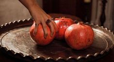 two pomegranates on a metal plate being held by a woman's hand