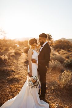 a bride and groom pose for a photo in the desert at their wedding day, while the sun is setting