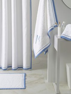 a white bathroom with blue trimmings on the shower curtain, and a personal monogrammed towel