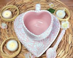 a pink heart shaped bowl and some candles on a wicker table