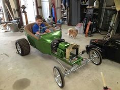 a young boy sitting in a green pedal car next to a brown dog on the floor