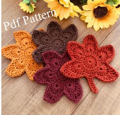 four crocheted flowers sitting on top of a wooden table next to sunflowers