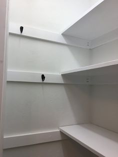 empty white shelves in the corner of a walk - in closet with black knobs