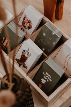 a wooden box filled with lots of cards on top of a table next to a potted plant