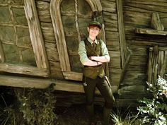 a man standing in front of a wooden structure with his arms crossed and wearing a hat