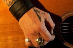 a man with tattoos on his arm holding an acoustic guitar and wearing a band around his wrist