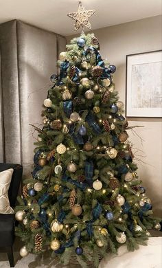 a christmas tree with blue and gold ornaments in a living room next to a couch