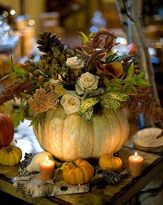 a large pumpkin decorated with flowers and candles sits on a table surrounded by other fall decorations