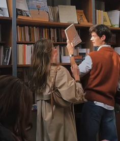 two people standing next to each other in front of a book shelf filled with books