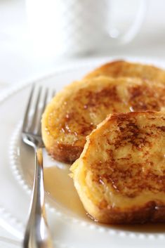 two pieces of french toast on a white plate with a fork and cup in the background