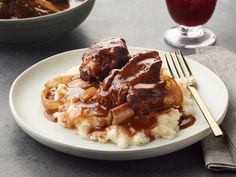 a white plate topped with meat and potatoes covered in gravy next to a glass of red wine