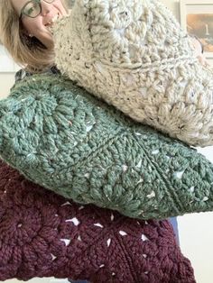 a woman holding three knitted pillows in front of her face