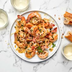 a white plate topped with shrimp next to two glasses of cream cheese and garlic bread