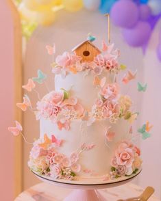 there is a white cake with pink flowers on it and a birdhouse topper