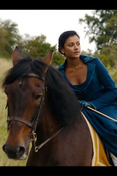 a woman riding on the back of a brown horse in a field with tall grass