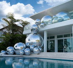 a large silver ball sculpture sitting next to a swimming pool in front of a house